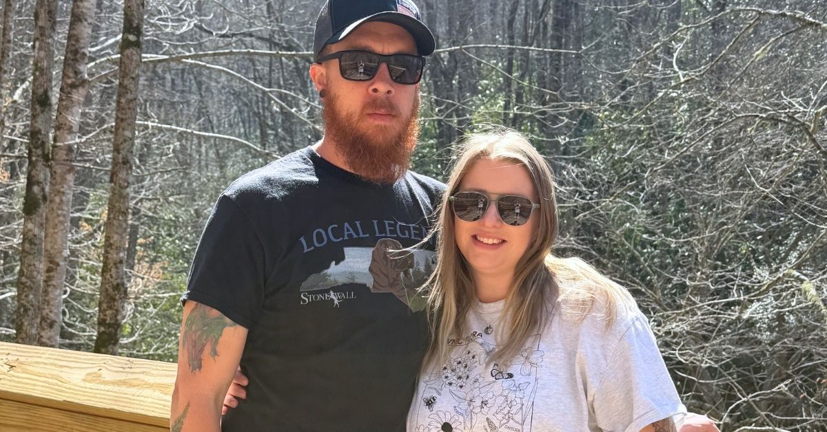 Two people standing outdoors with forest background