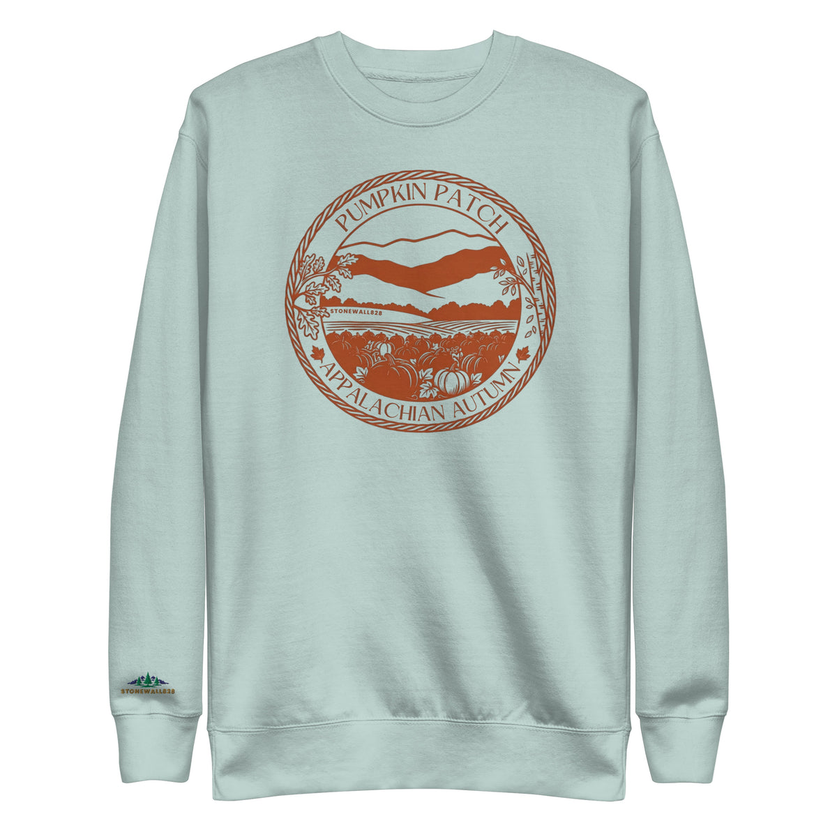 A light mint green crewneck sweatshirt featuring a circular orange graphic on the chest that reads 'Pumpkin Patch Nепalagachan Autumn' with an illustration of a mountain and autumn landscape. A small orange graphic is also printed on the left sleeve cuff.